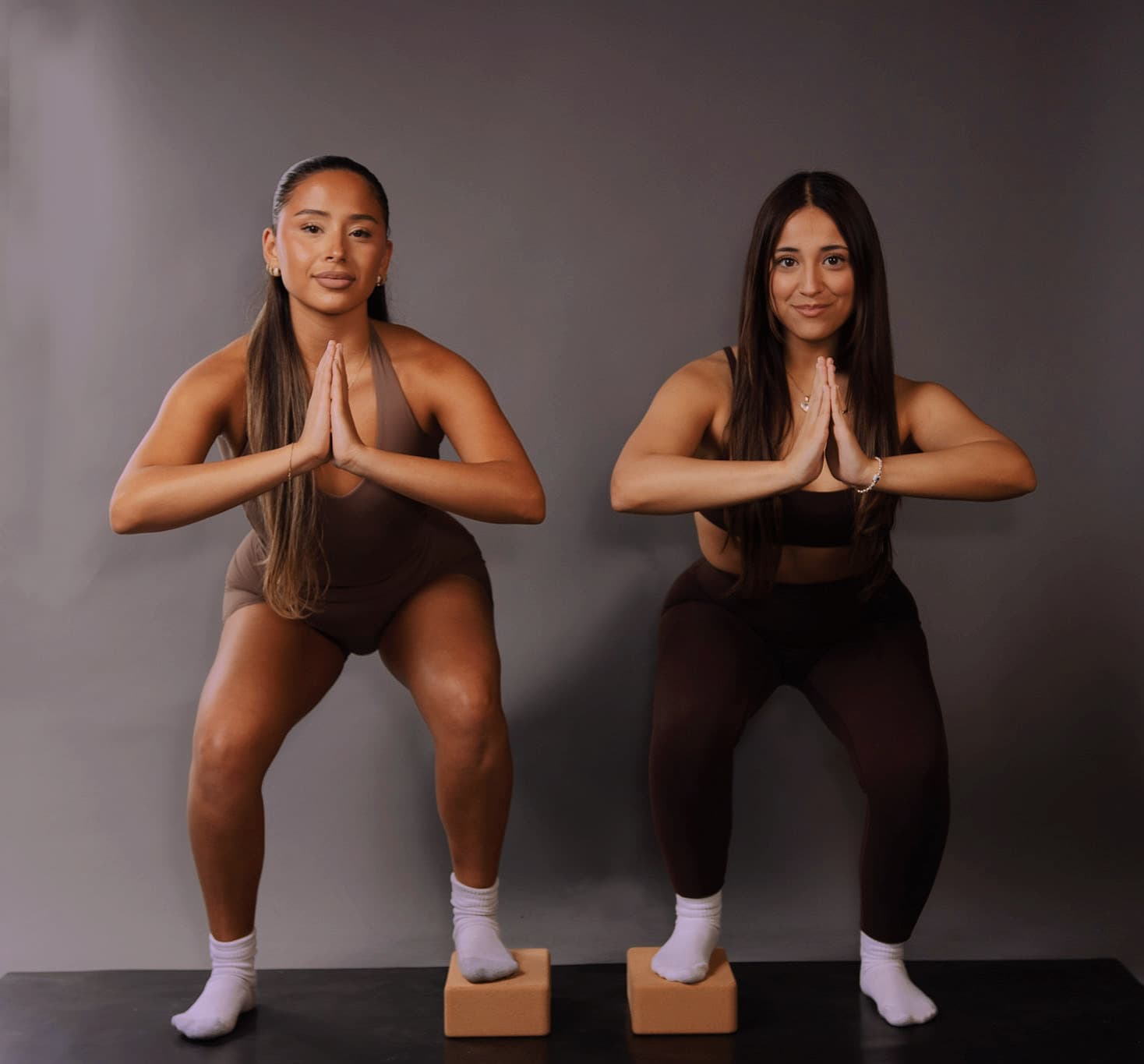 Two members mid-class, in a low squat with hands at the chest, on mats with cork blocks.